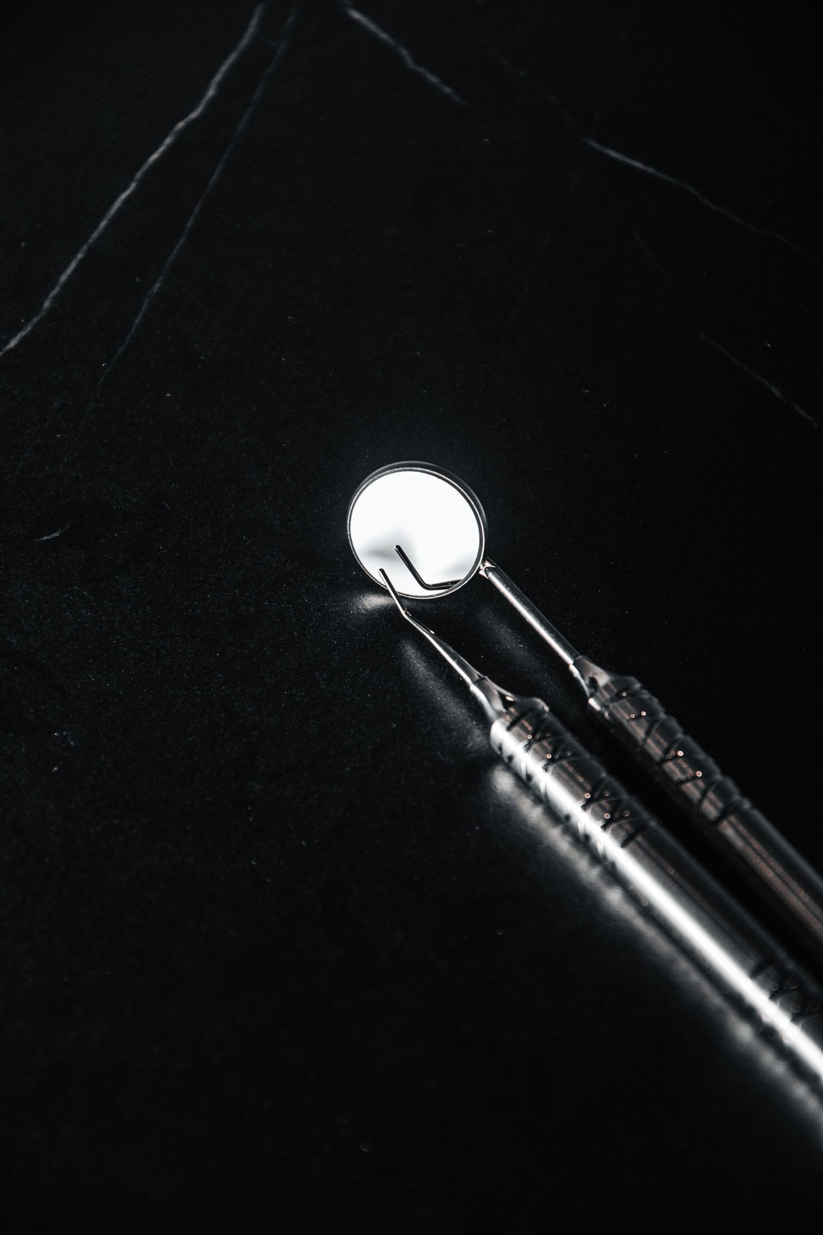 Detailed view of dental mirror and probe on a black surface, emphasizing cleanliness.